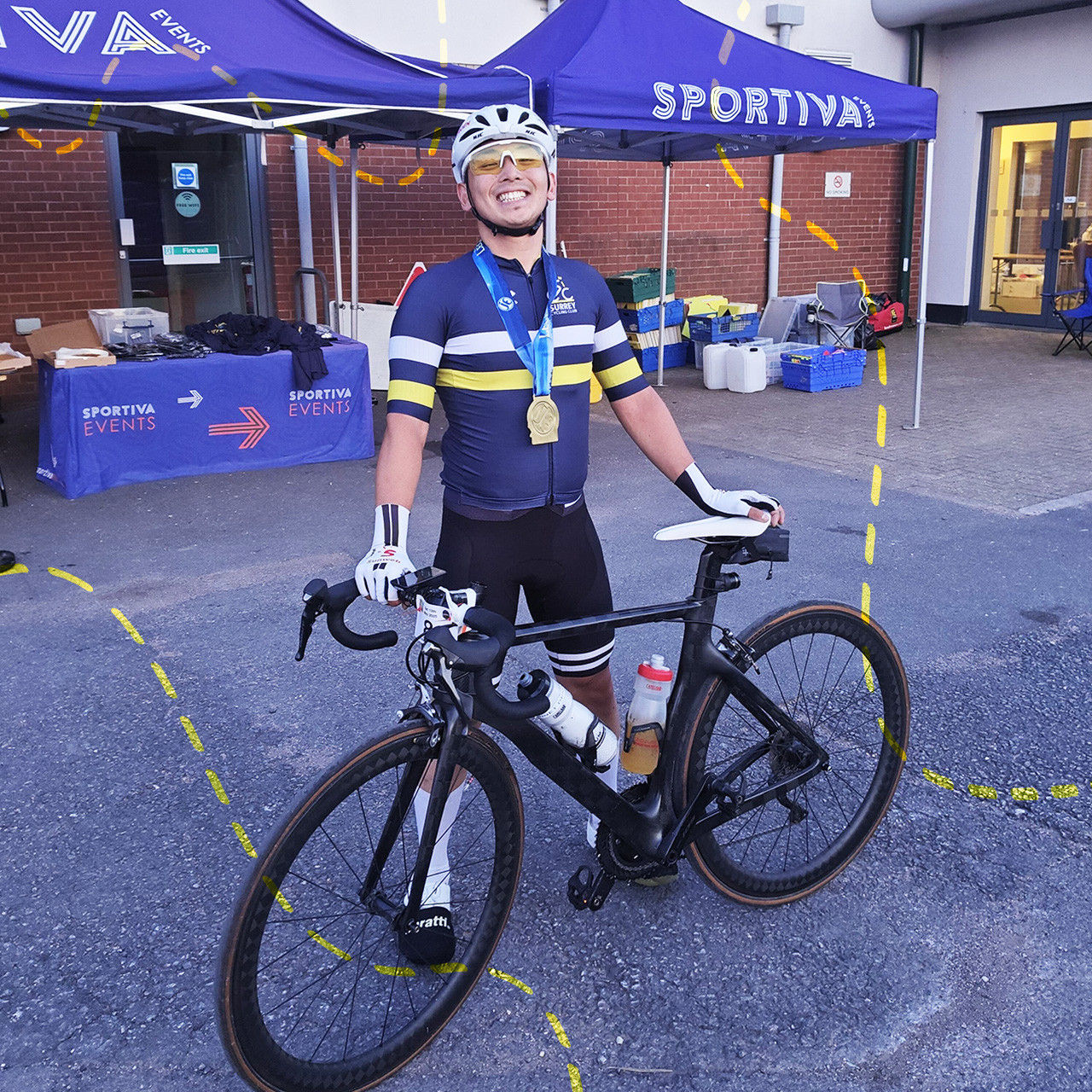 A cyclist in full gear stands with a bike, smiling and wearing a medal, in front of SPORTIVA EVENTS tents at an outdoor event.