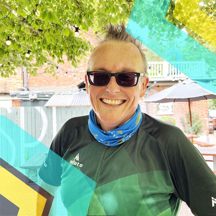 A man in a Surrey Cycling Club jersey is smiling in front of a sign.